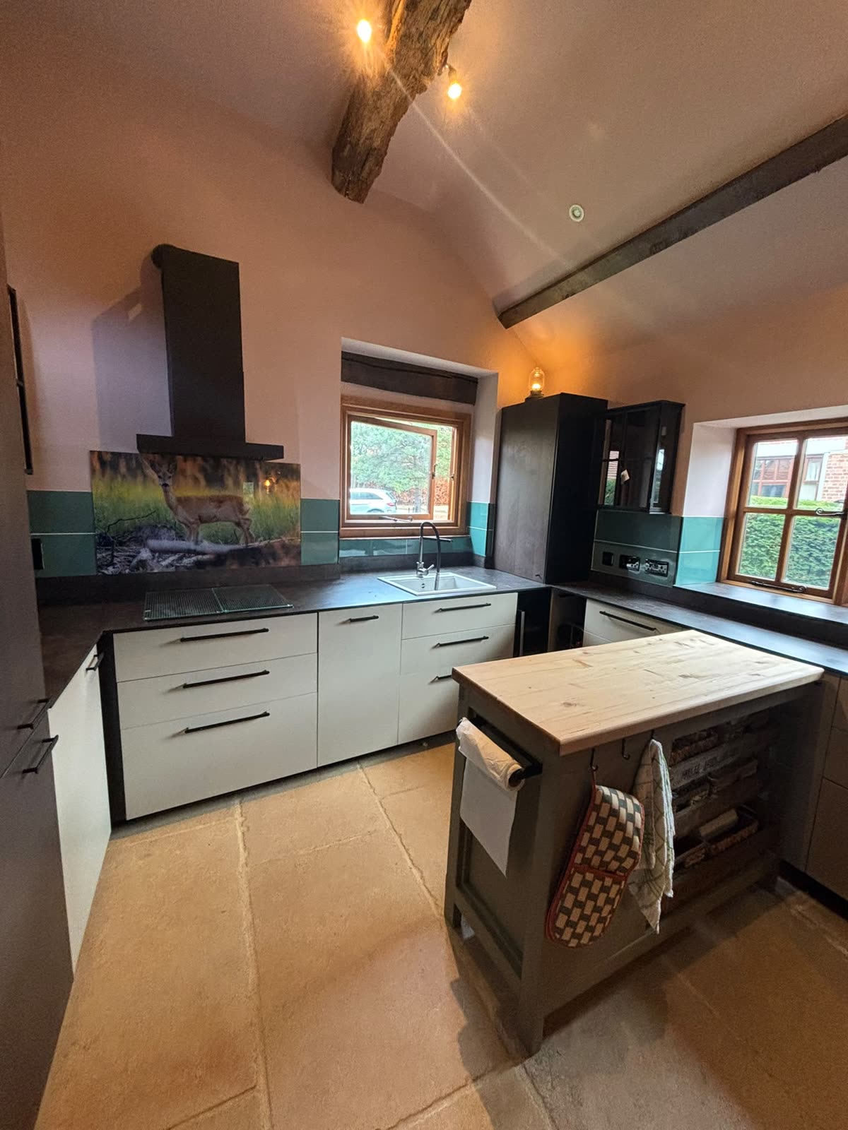 Kitchen with dark worktops, green splashback and beamed ceiling